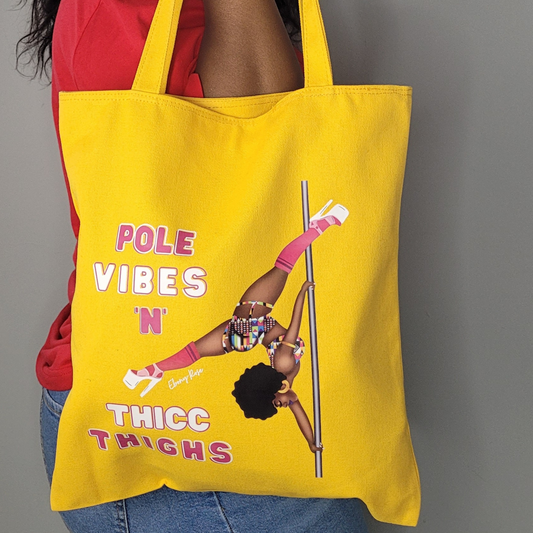 yellow tote bag featuring a black pole dancer wearing bright African inspired Afrocentric garter pole shorts and sports top Bright pink knee socks and clear platform heels in an extended butterfly pose with slogan affirmation pole vibes n thicc vibes
