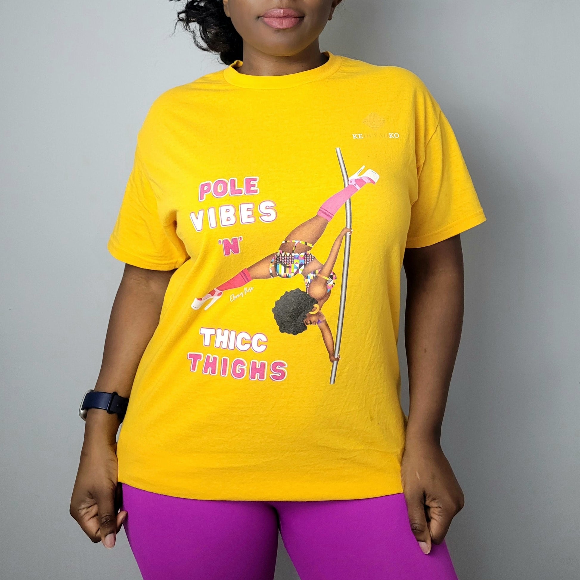 Yellow unisex t-shirt  featuring a black pole dancer wearing bright African inspired Afrocentric garter pole shorts and sports top. Bright pink knee socks and clear platform heels in an extended butterfly pole pose with slogan affirmation pole vibes n thicc vibes