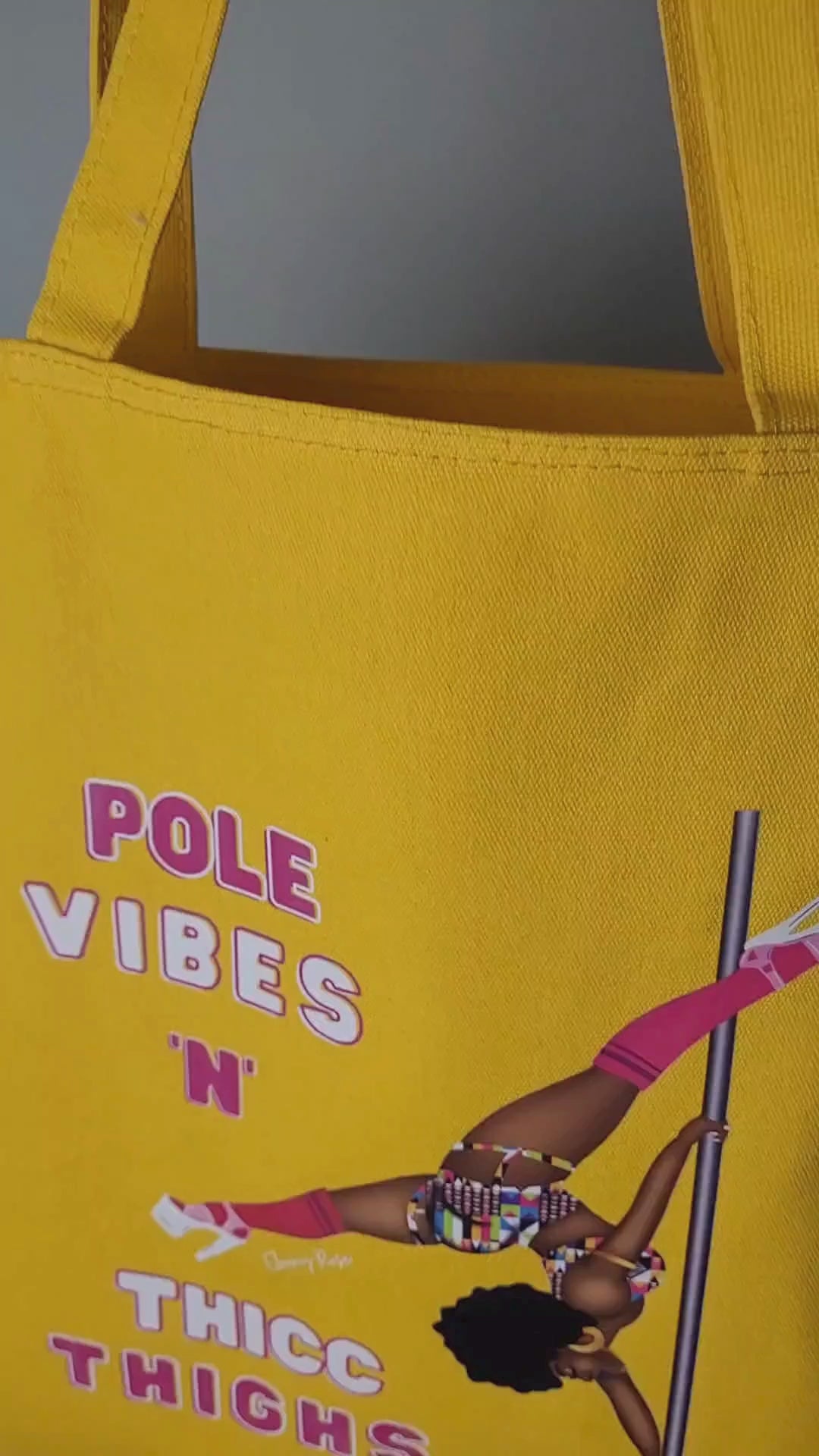 yellow tote bag featuring a black pole dancer wearing bright African inspired Afrocentric garter pole shorts and sports top Bright pink knee socks and clear platform heels in an extended butterfly pose with slogan affirmation pole vibes n thicc vibes